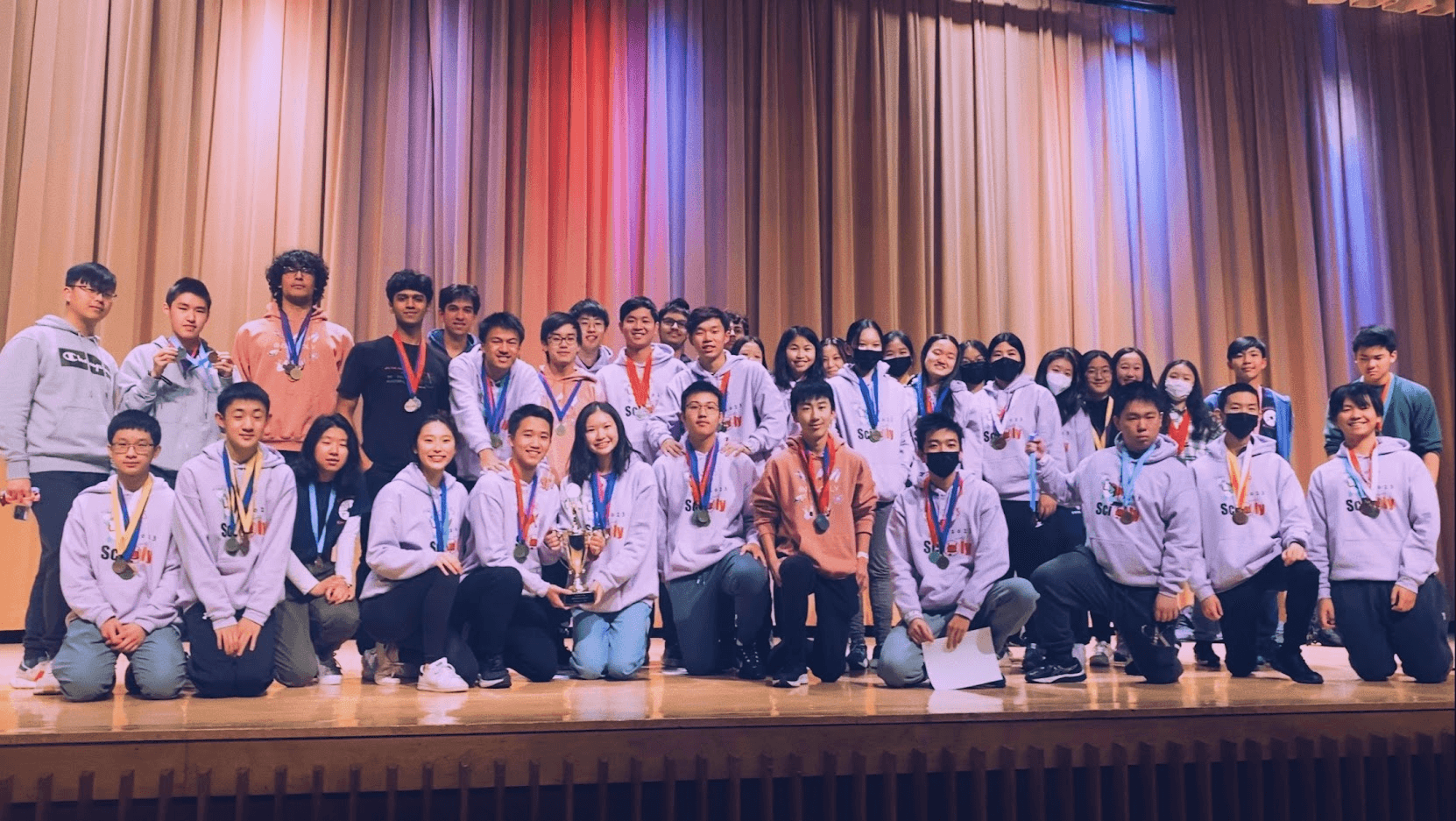 The whole team in matching hoodies, wearing medals, posed on an auditorium stage